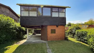 Haus mit Holzfassade und kleinem Vorgarten unter blauem Himmel.
