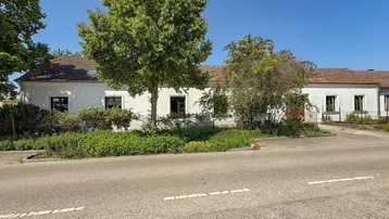 Weißes Gebäude mit traditioneller Architektur, umgeben von Bäumen und einer Straße.