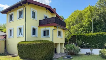 Gelbes Haus mit rotem Dach, umgeben von einem gepflegten Garten und grünen Hecken.