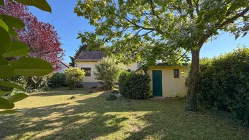 Gartenbereich mit Rasenfläche und Bäumen vor einem Haus unter blauem Himmel.