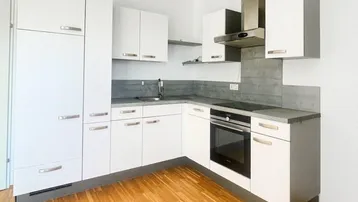 Moderne Einbauküche mit weißen Schränken, Edelstahlgeräten und hellem Holzfußboden.