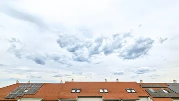 Reihenhäuser mit roten Ziegeldächern und Solaranlagen unter bewölktem Himmel.
