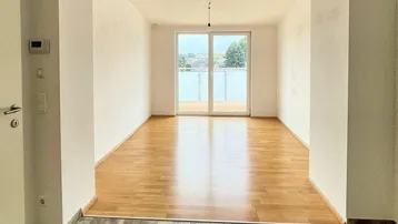 Helles, leeres Wohnzimmer mit Holzboden und Zugang zu einem Balkon, bereit zur Einrichtung.