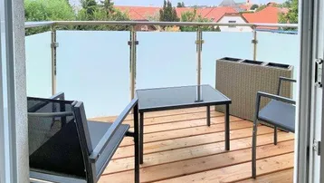 Balkon mit Holzboden, Glasgeländer und Blick auf die umliegende Bebauung.