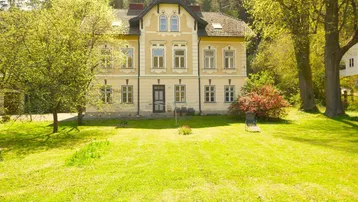 Großzügiger Gartenbereich vor einem charmanten, historischen Gebäude mit klassischer Architektur und vielen Bäumen.