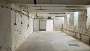 Großer, leerer Kellerraum mit Betonboden und sichtbaren Leitungen, Wände zeigen Abnutzungsspuren.