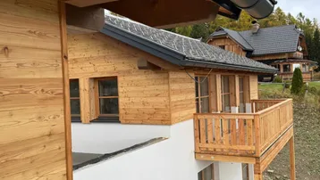 Nahaufnahme eines neuen Holzchalets mit Balkon und Blick auf die umliegende Natur.