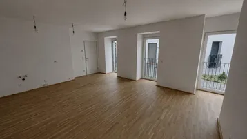 Heller, leerer Wohnraum mit Parkettboden und Zugang zu französischen Balkonen in einem Neubau.