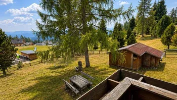 Panoramablick vom Holzbalkon auf die umliegende Berglandschaft mit Wald und Gartenhäuschen.