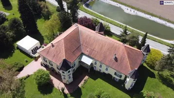 Luftaufnahme eines weitläufigen Anwesens mit historischem Gebäude, umgeben von viel Grün und einem Teich.