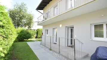 Außenansicht des Gebäudes mit gepflegtem Gartenbereich, Terrasse und Balkon im Obergeschoss.