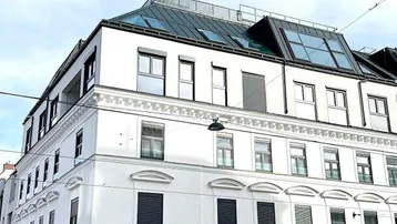 Modernes Eckgebäude mit weißer Fassade, großen Fenstern und Dachausbau in städtischer Umgebung.