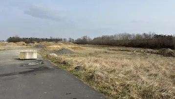 Weites unbebautes Grundstück mit Erdhügeln und Schotter, bereit für die Bebauung, unter bewölktem Himmel.