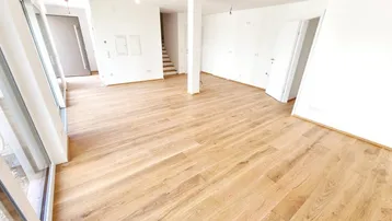 Heller Wohnbereich mit neuem Holzparkett, weißen Wänden und Zugang zu einer Treppe.