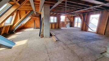 Unausgebauter Dachbodenbereich mit sichtbaren Holzbalken und Dachfenstern, bereit für den Ausbau.