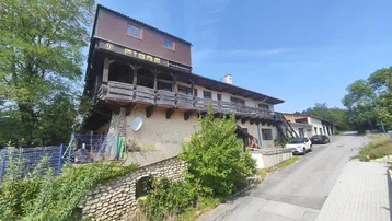 Altes Gebäude mit Holzverkleidung und Balkonen, umgeben von Bäumen und einer Straße.