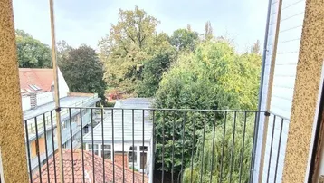 Kleiner Balkon mit Holzboden und Blick ins Grüne sowie auf umliegende Dächer.