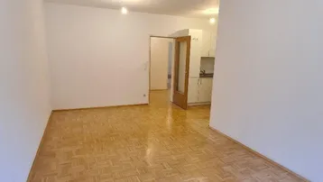 Geräumiger Wohnbereich mit Parkettboden und Zugang zu einer angrenzenden Küche.