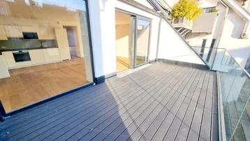 Geräumige Dachterrasse mit Holzboden und Glasgeländer, direkt zugänglich von der modernen Küche.