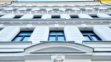 Historische Fassade eines Altbaus mit aufwendigen Stuckverzierungen und blauen Fenstern.