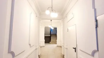 Langer, heller Flur mit Stuckelementen an den Wänden und Decken, der zu einem Treppenhaus führt.