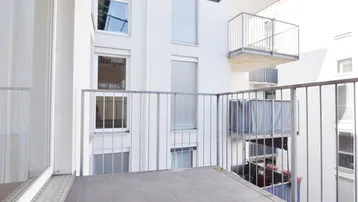 Heller Balkon mit Fliesenboden und Metallgeländer, umgeben von moderner Architektur.