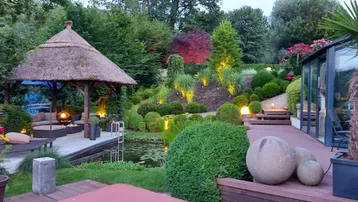 Malerischer Garten mit Strohdach-Pavillon, Teich und beleuchteten Pflanzen für entspannte Abende.