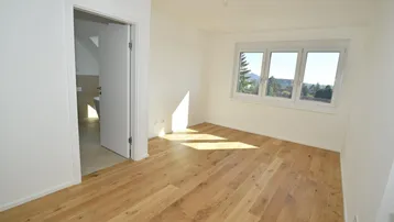 Helles Zimmer mit Holzboden und Fenster, das einen grünen Ausblick auf die Umgebung bietet.
