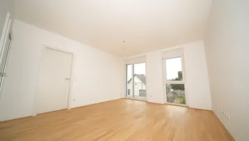 Heller, leerer Raum mit hellem Parkettboden und Zugang zu einem Balkon oder einer Terrasse.