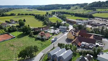 Weitläufige Luftaufnahme der Reihenhäuser eingebettet in die grüne Landschaft mit Feldern und Wäldern.