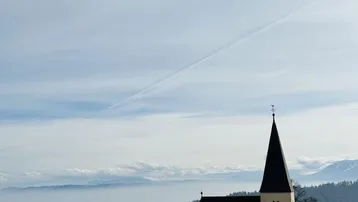 Kleine Kirche auf einem Hügel mit weitem Blick über eine hügelige Landschaft und Berge im Hintergrund.