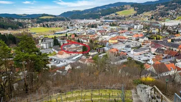 Luftaufnahme einer Stadt mit umliegenden Bergen und Weinbergen, das Objekt ist rot markiert.