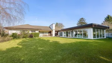 Weitläufiger Garten mit gepflegtem Rasen und moderner Glaserweiterung des Hauses.