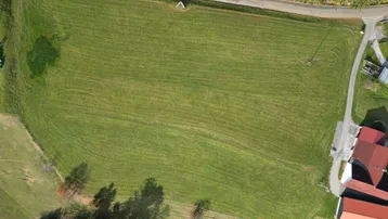 Luftaufnahme eines großen grünen Grundstücks mit angrenzender Straße und Wald in ländlicher Umgebung.