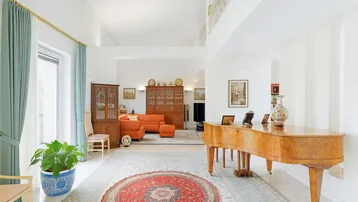 Geräumiges Wohnzimmer mit hohen Decken, einem Flügel und traditionellen Teppichen, durchflutet von natürlichem Licht.