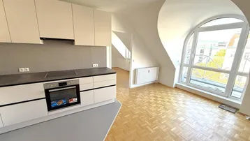 Helle Dachgeschosswohnung mit moderner Einbauküche, Parkettboden und großem Bogenfenster.