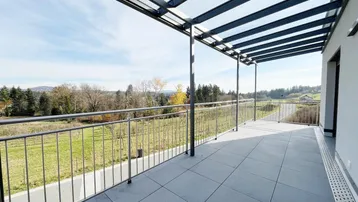 Großer überdachter Balkon mit Fliesenboden und weitem Blick ins Grüne und die Landschaft.