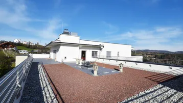 Weitläufige Dachterrasse mit dekorativen Elementen, Kiesflächen und Panoramablick über die Landschaft.