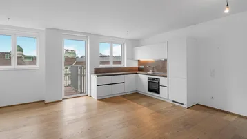 Heller offener Wohnbereich mit integrierter Küche, Holzboden und Zugang zum Balkon.