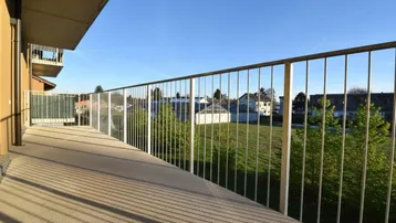 Geräumiger Balkon mit Metallgeländer und weitem Blick ins Grüne unter blauem Himmel.