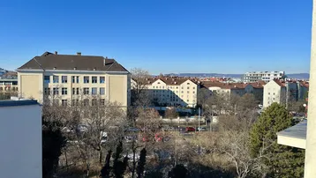 Weitläufiger Blick über die Stadt mit Gebäuden und Bäumen unter klarem, blauem Himmel.