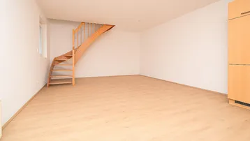 Leerer Raum mit Holztreppe, Laminatboden und viel natürlichem Licht.
