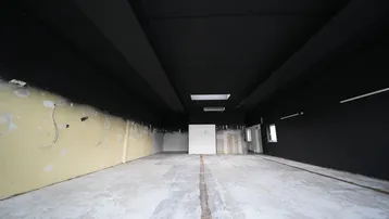 Weitläufiger Gewerberaum mit schwarzer Decke und Wänden, hellem Betonboden und Oberlicht für Tageslicht.