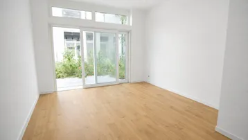 Helles, leeres Zimmer mit großen Schiebetüren und Zugang zu einem kleinen Außenbereich.
