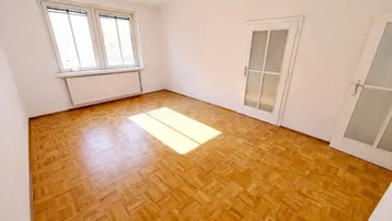 Helles Zimmer mit Parkettboden und zwei Türen, durchflutet von natürlichem Sonnenlicht.