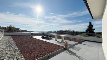 Sonnige Dachterrasse mit weitem Blick über die Landschaft und dekorativen Kiesflächen.