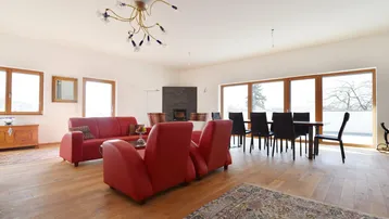 Geräumiger Wohn- und Essbereich mit Holzboden, roten Sofas und großen Fenstern.