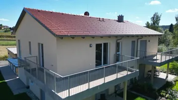 Helles, modernes Einfamilienhaus mit großzügigen Balkonen, einer Terrasse und gepflegtem Garten, umgeben von grüner Landschaft und mit Weitblick.