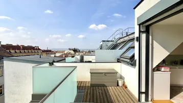 Geräumige Dachterrasse mit Holzboden, Glasgeländer und weitem Blick über die Stadt.