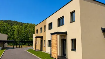 Moderne Reihenhäuser mit beiger Fassade, dunklen Fenstern und Holzdetails in einer grünen Umgebung.